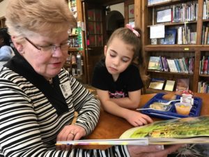A woman from the community reads with an elementary student in the library during lunch