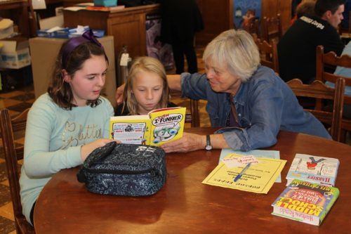 A woman from the community reads with elementary students in the library during lunch