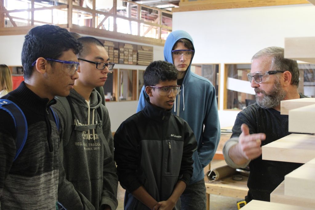 a shop employee shows students the pieces of wood he is manufacturing