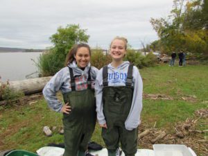 two girls wearing chest waders by river