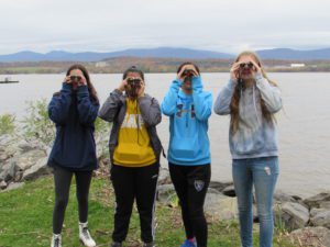 four girls holding binoculars by river