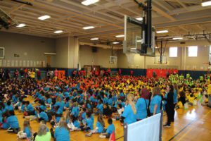 gymnasium filled with students and teachers in colorful t-shrits