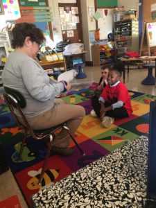a woman reads to elementary students seated on floor
