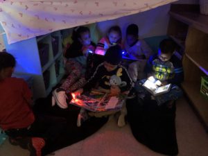elementary students read together in a blanket fort