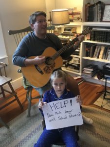 kid holding paper with handwritten message while dad plays guitar