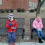 two elementary students seated on a bench enjoying donuts
