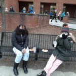 two elementary students seated on a bench enjoying donuts and hot cocoa