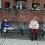 two elementary students seated on a bench enjoying donuts