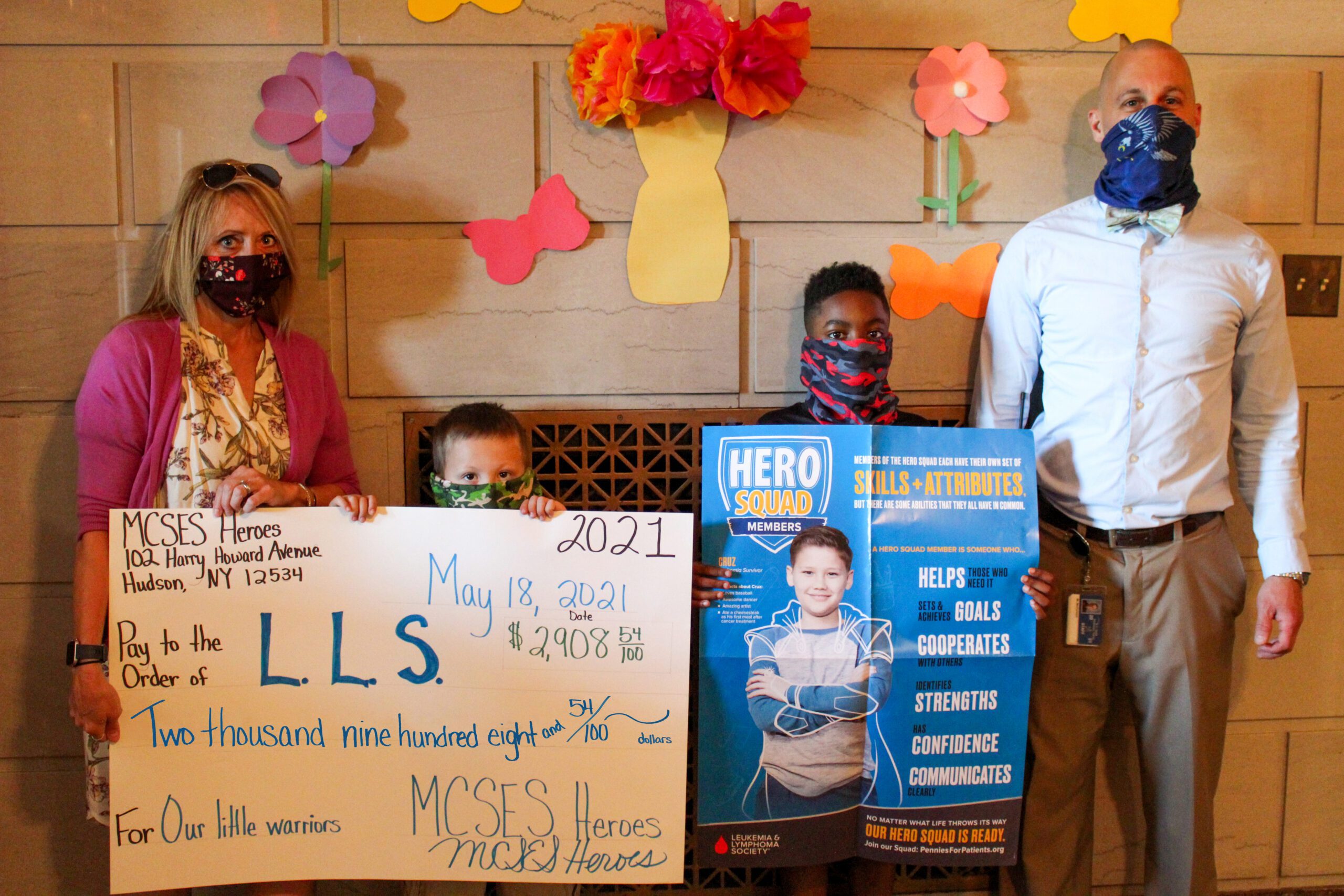 two elementary boys standing between adults and holding a big check totaling $2,908