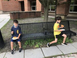 two elementary students seated on bench enjoying donuts