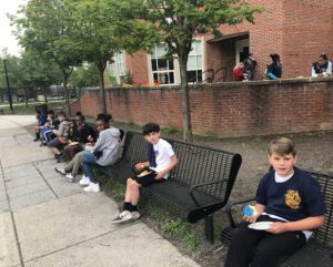 several elementary students seated on benches enjoying donuts