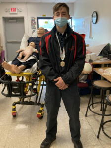 senior Jaxon Haigh poses with adult and baby CPR dummies on a stretcher
