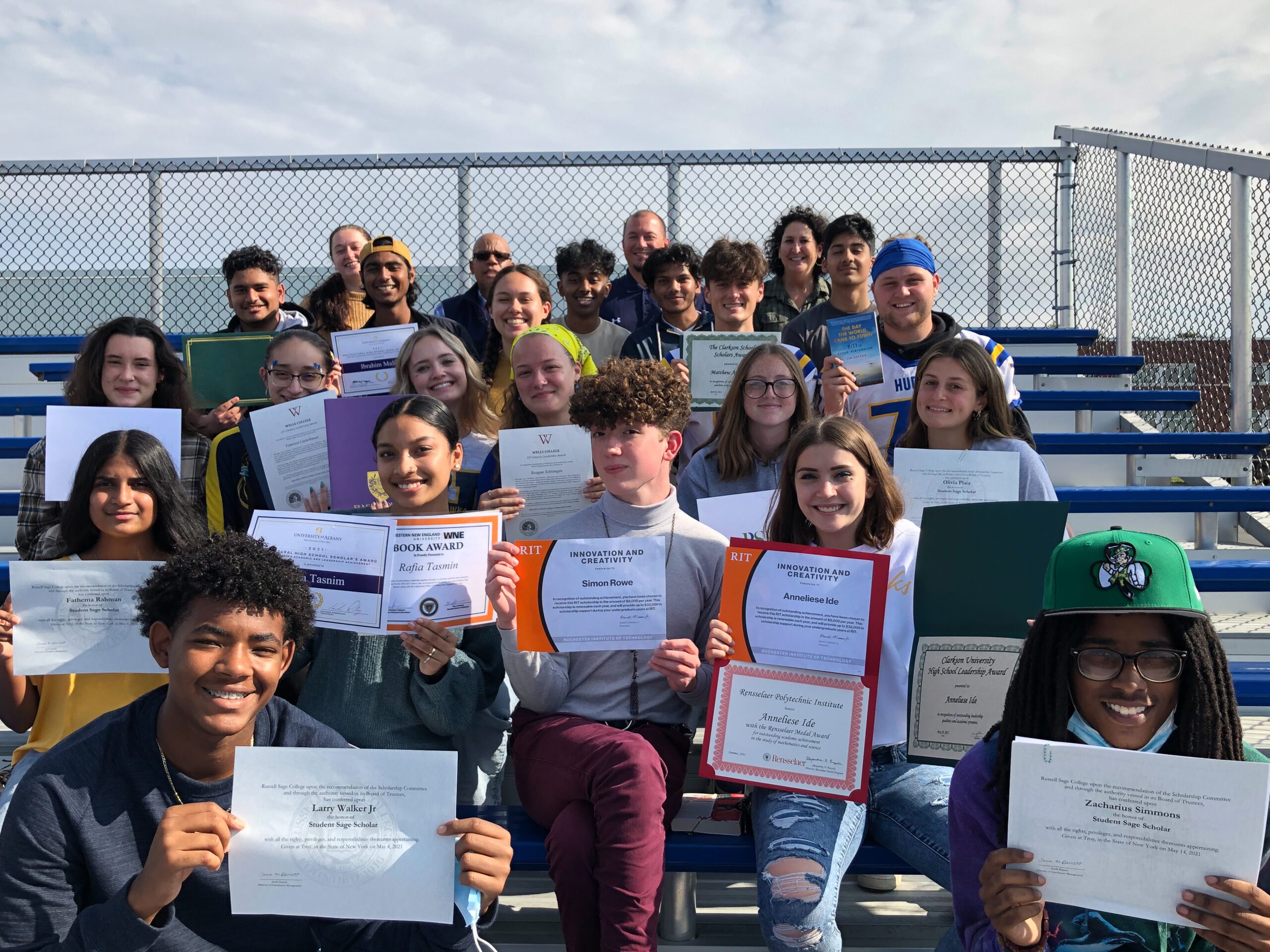 a group of high school students holding up certificates while seated on outdoor bleachers