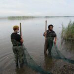 two high school boys wearing chest waders prepare to walk a seine net into the river