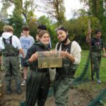two high school girls wearing chest waders hold a container of river water