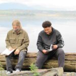 two high school boys with notes sitting on a log by the Hudson River