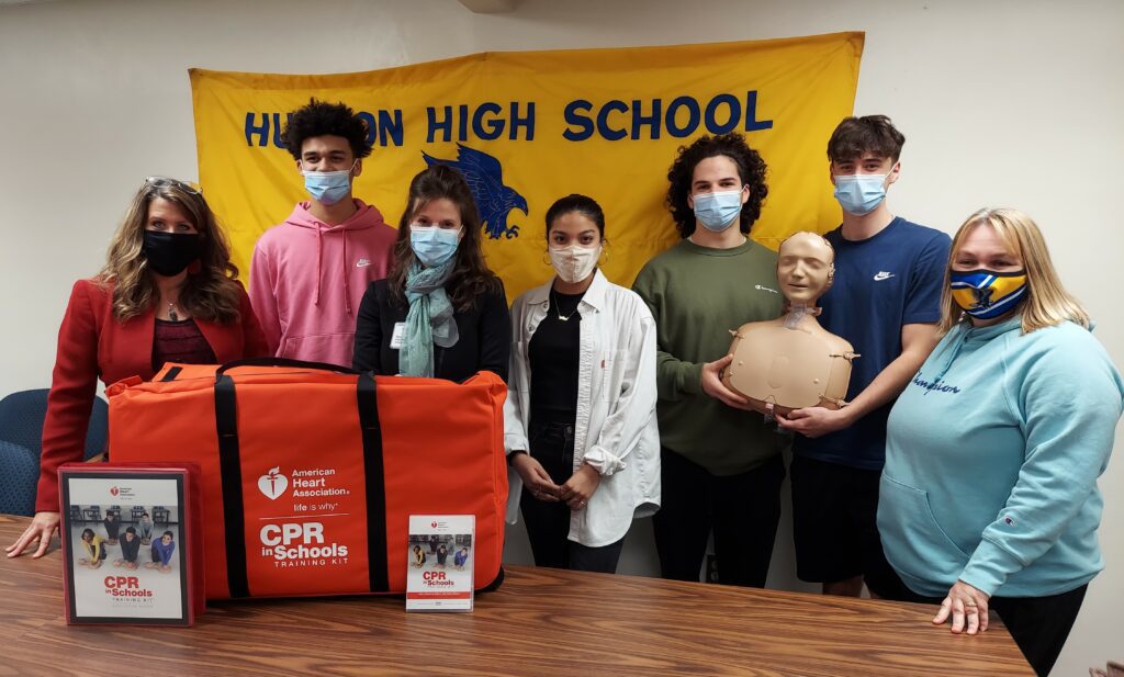 an ethnically and racially diverse group of students and adults show off a CPR in Schools kit