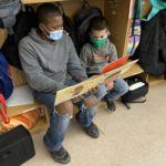 an older elementary boy reads to a younger elementary boy in a cubby