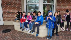 10 elementary students of differing genders and ethnic backgrounds sit on a concrete bench