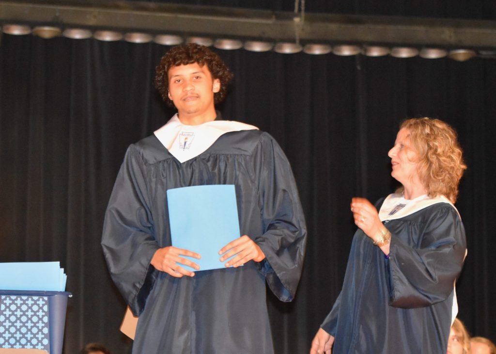 tan skinned high school boy on auditoriun stage whearing blue robe and white stole for National Honor Society