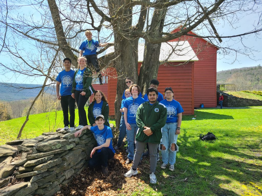 10 high school students outside by a tree and red barn; they are wearing blue t-shirts with tree graphics