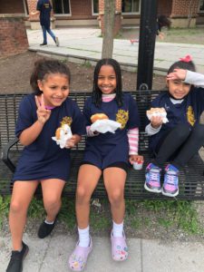 three elementary school girls eating breakfast while seated on a bench outside the school