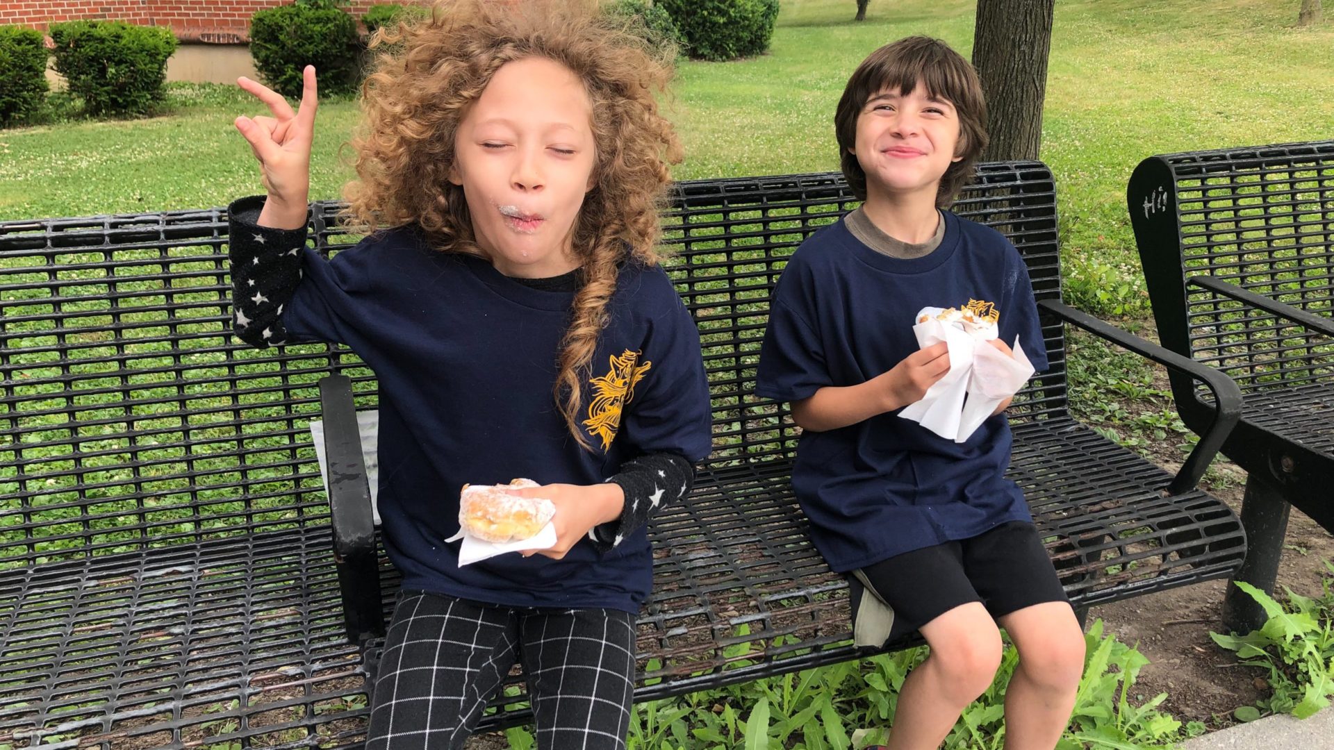 two elementary school students eating breakfast while seated on a bench outside the school