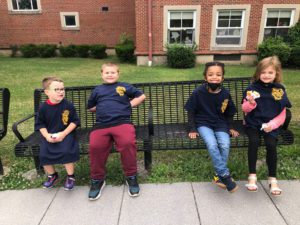 two elementary school boys and two girls seated on a bench outside the school